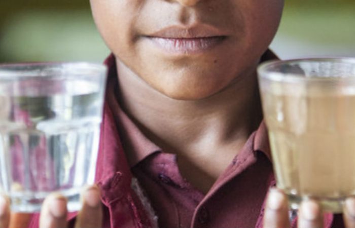 A student holds two glasses of water to show the difference in water quality in her school in PNG